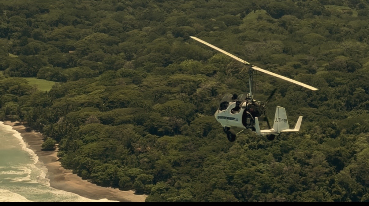 Autogiro en vuelo junto al bosque y la costa